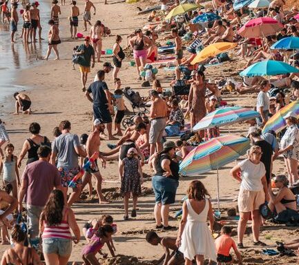 Vibrant scene of people enjoying a sunny day at a crowded beach, with colorful umbrellas and lively activities.